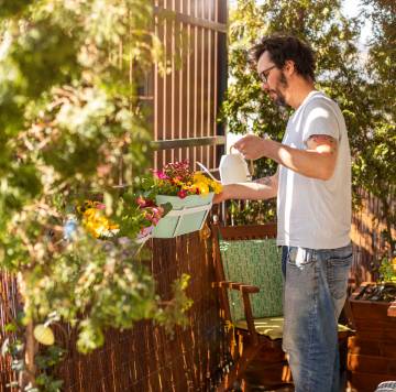 un hombre riega una jardinera en una terraza.