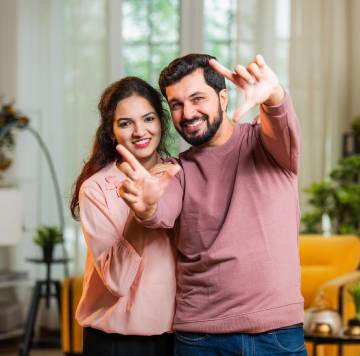 una pareja feliz mirando a la cámara y haciendo un gesto con las manos.
